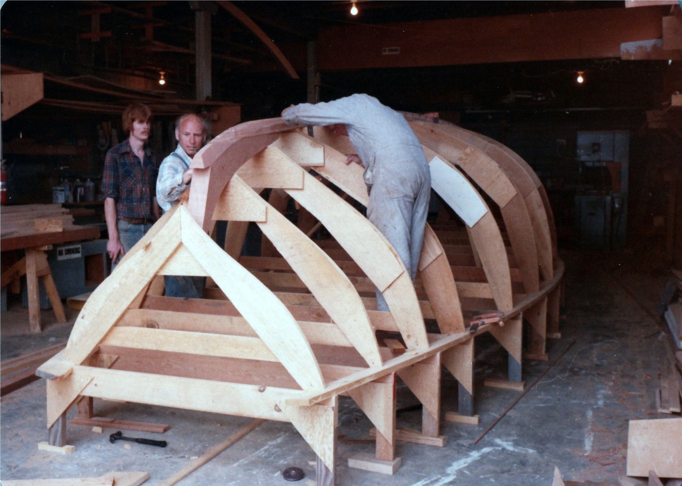 Three men at the upturned molds and frames of the hull in the boatshop