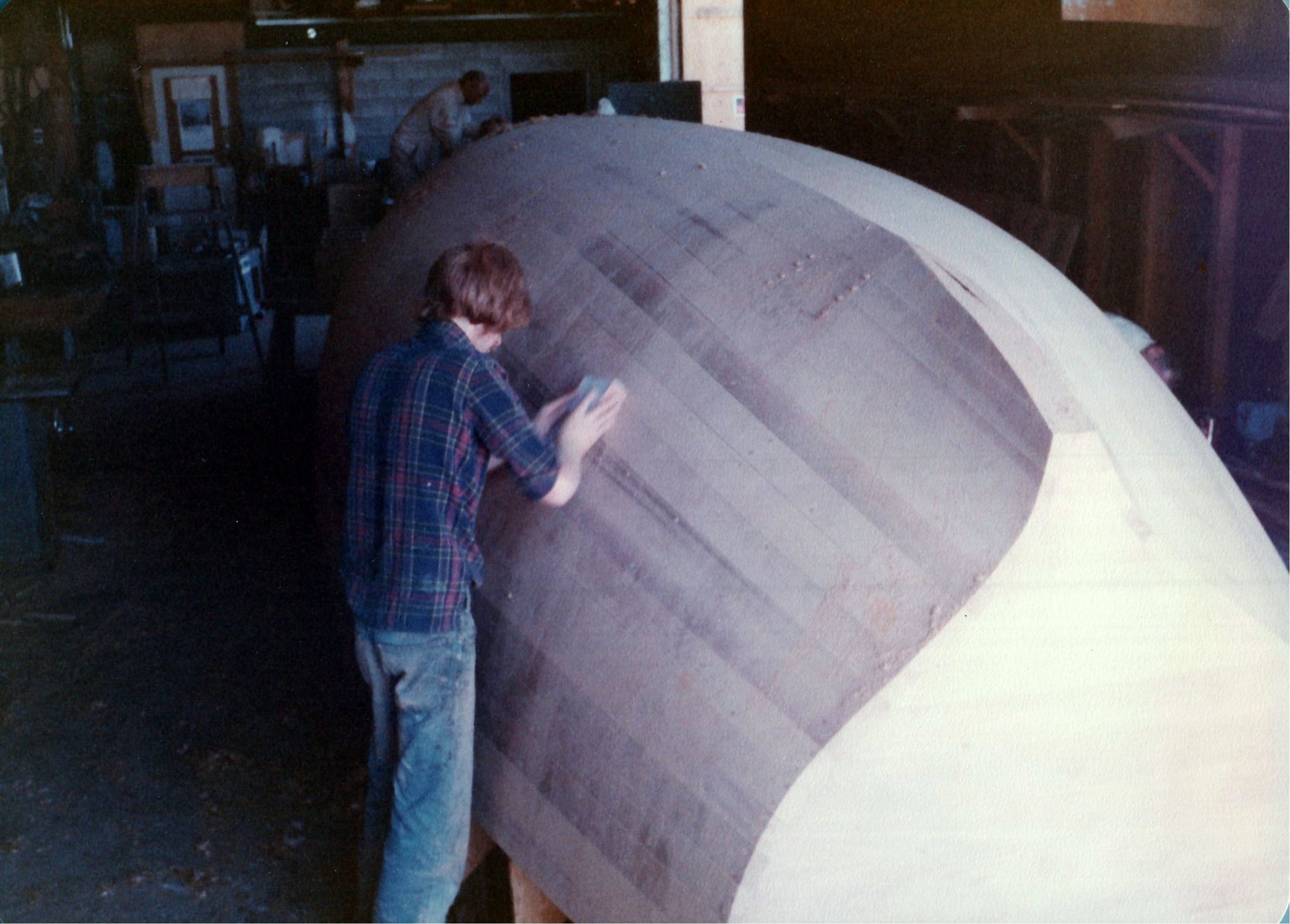 A man fairing the planked hull by hand