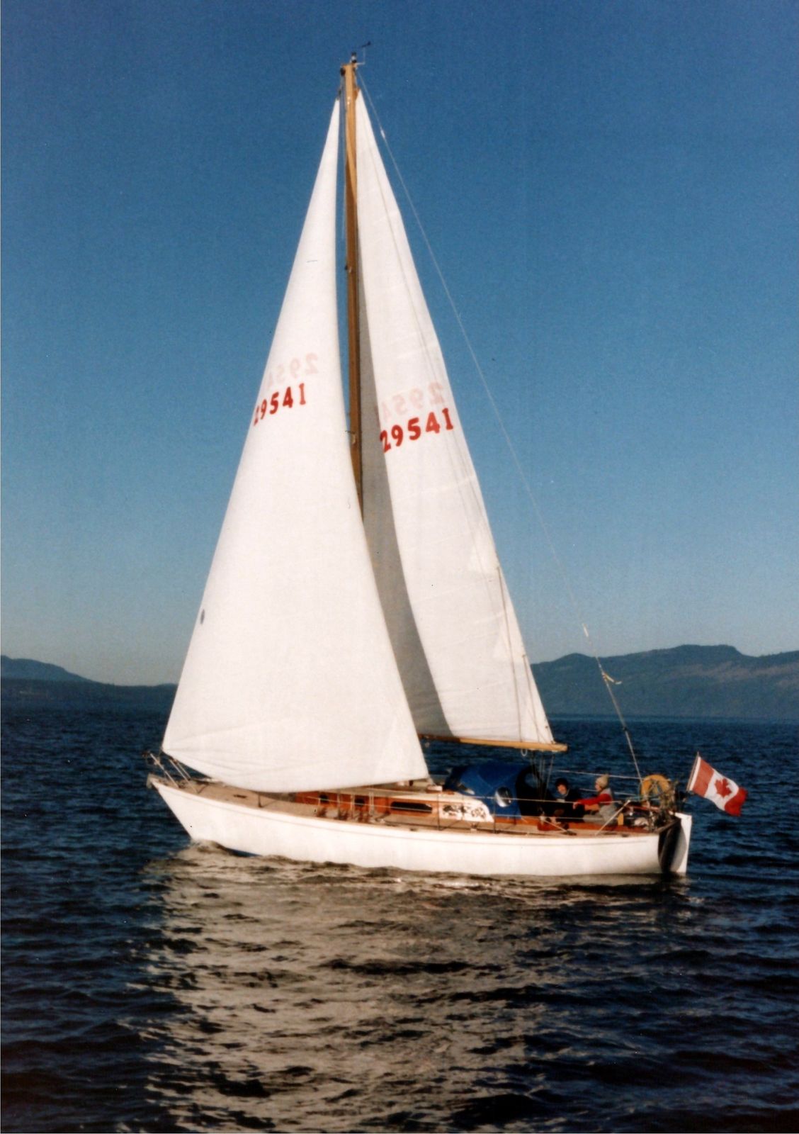 Jura under full sail on a blue day, flying the Canadian flag