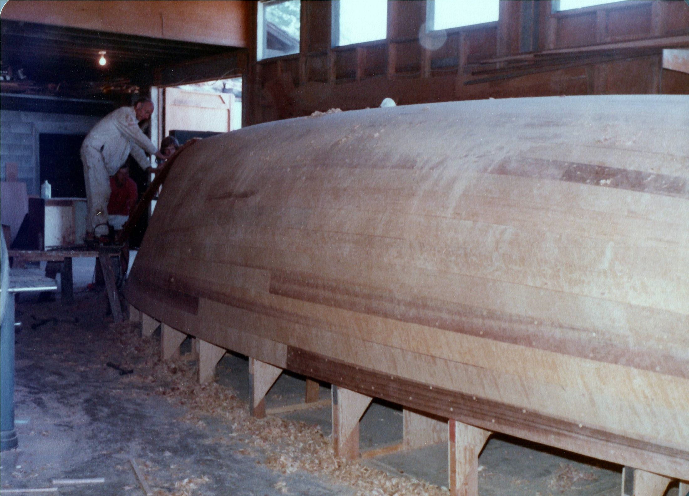 The faired hull, long and pale, shavings on the floor