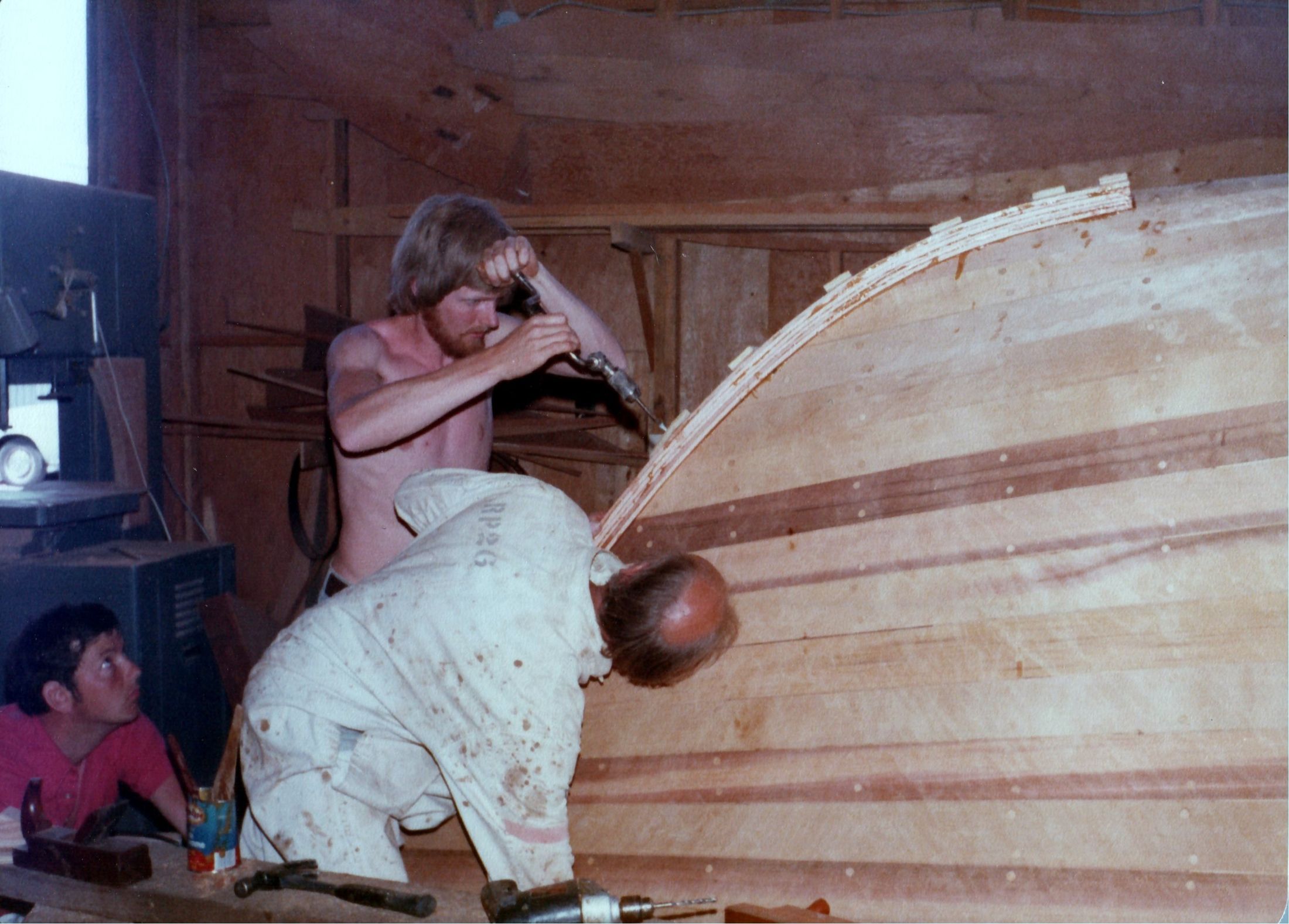 Two men at the stem, one in white overalls bent over the planking