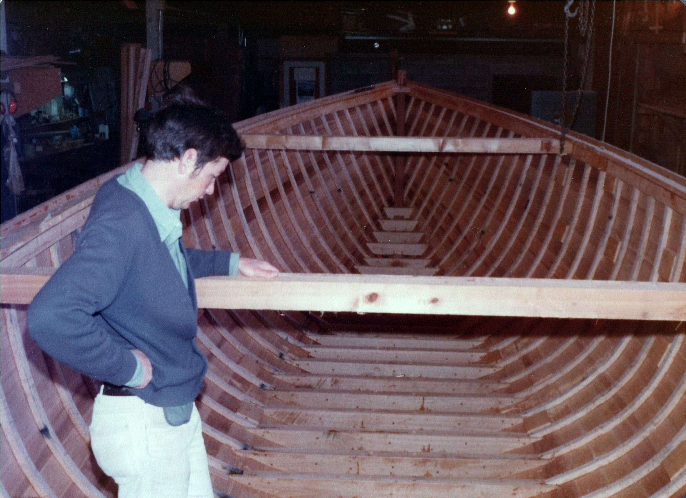 A man leaning on a beam across the open hull, frames and floors below