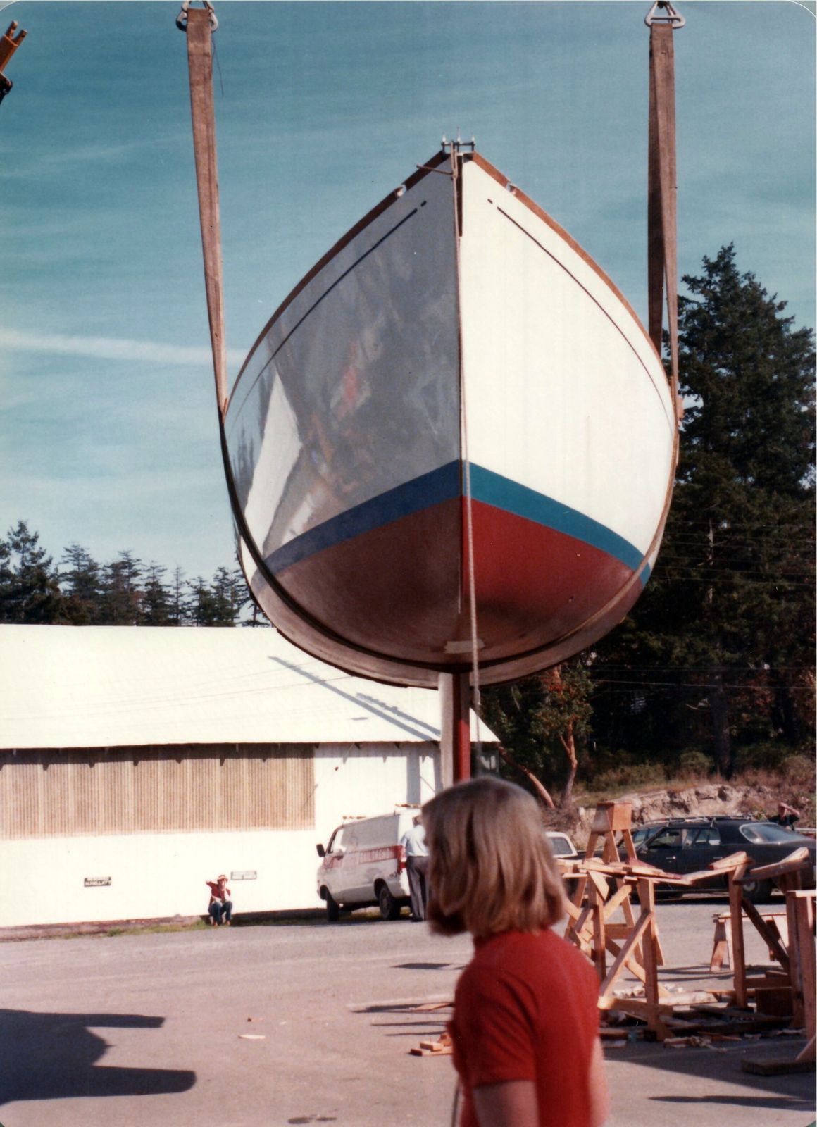 The hull hanging from the crane, a woman in red looking up