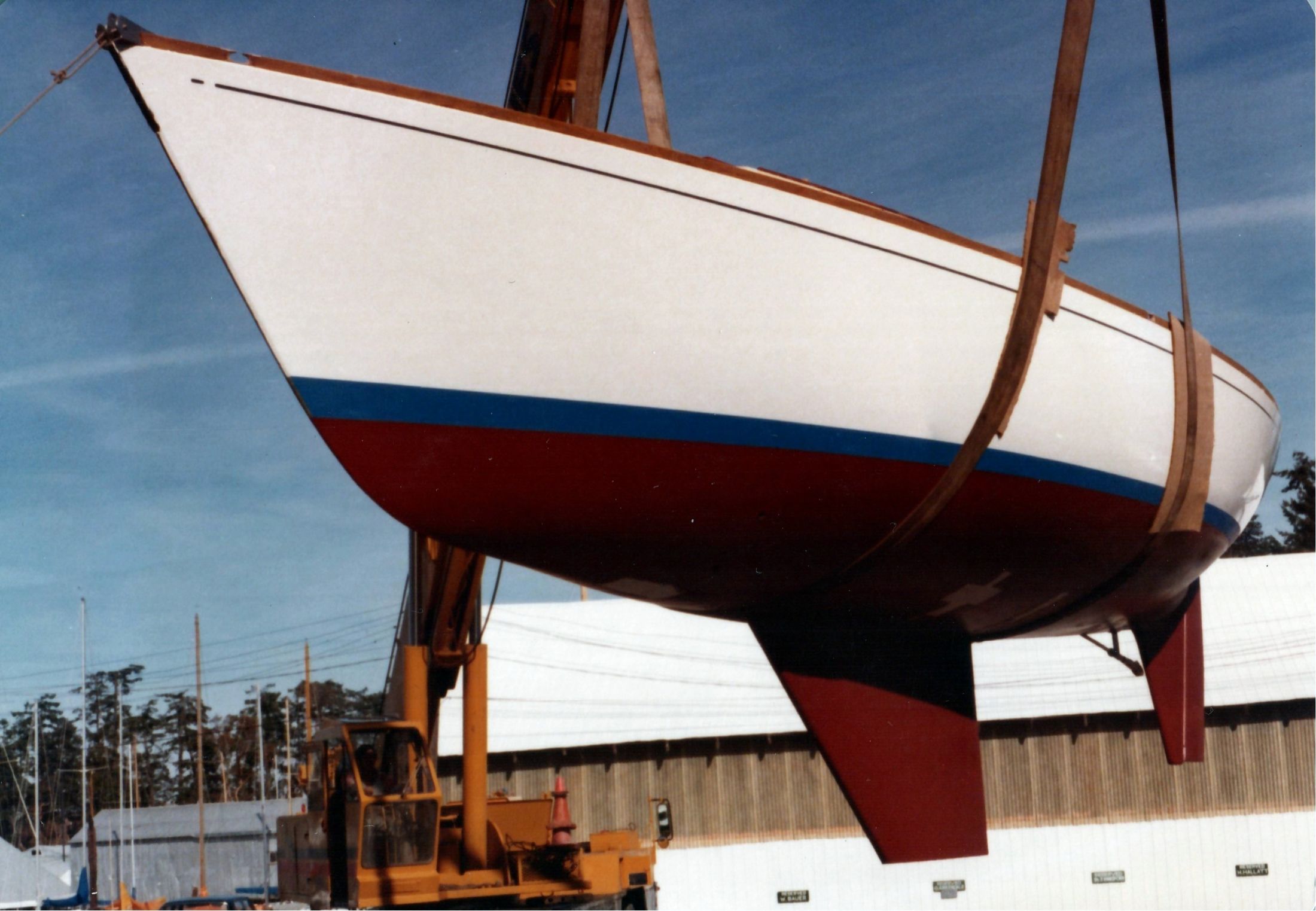The hull in the slings against a bright sky, the fin keel and rudder clear