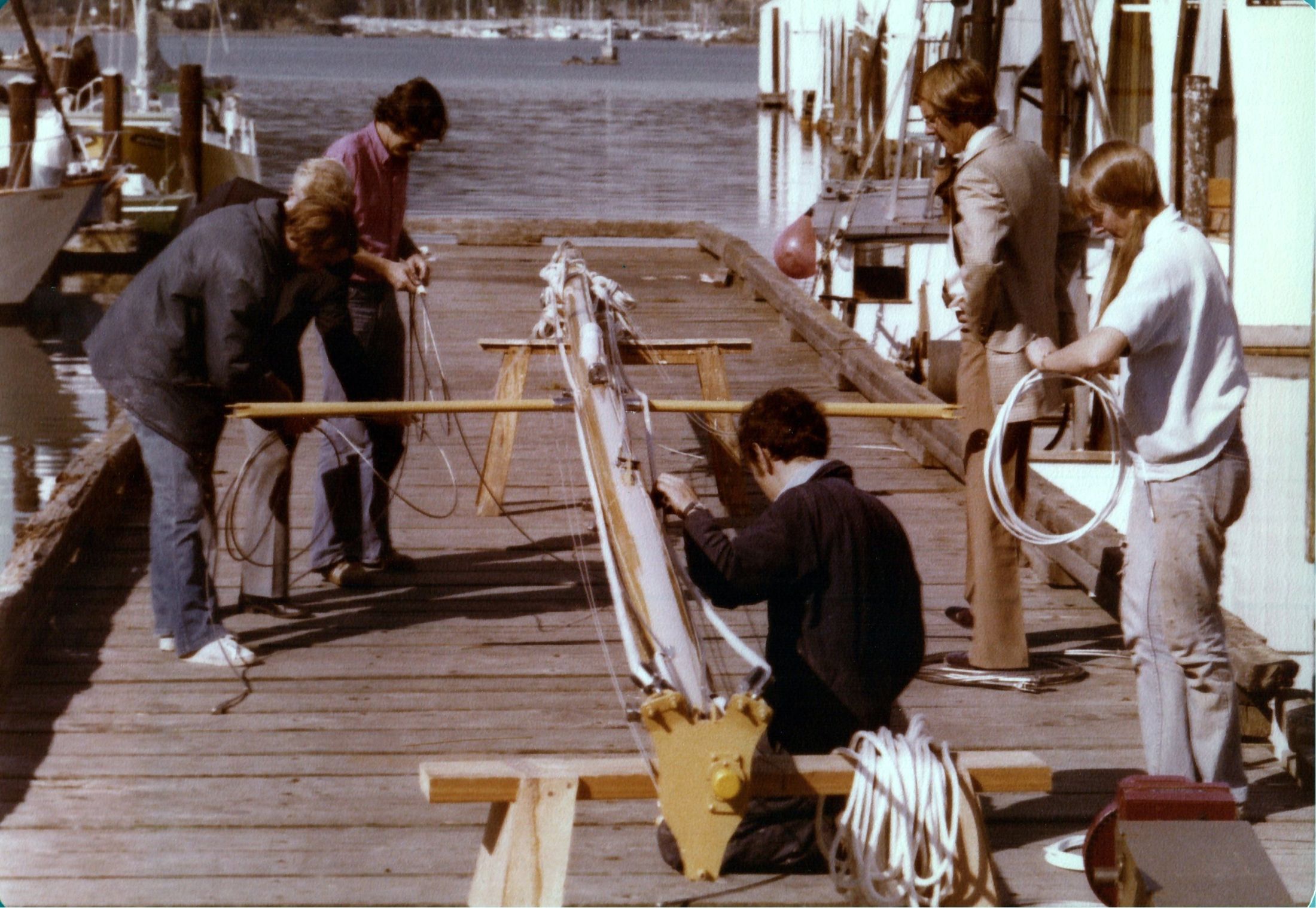 Rigging the mast on the dock, four people at the spreaders