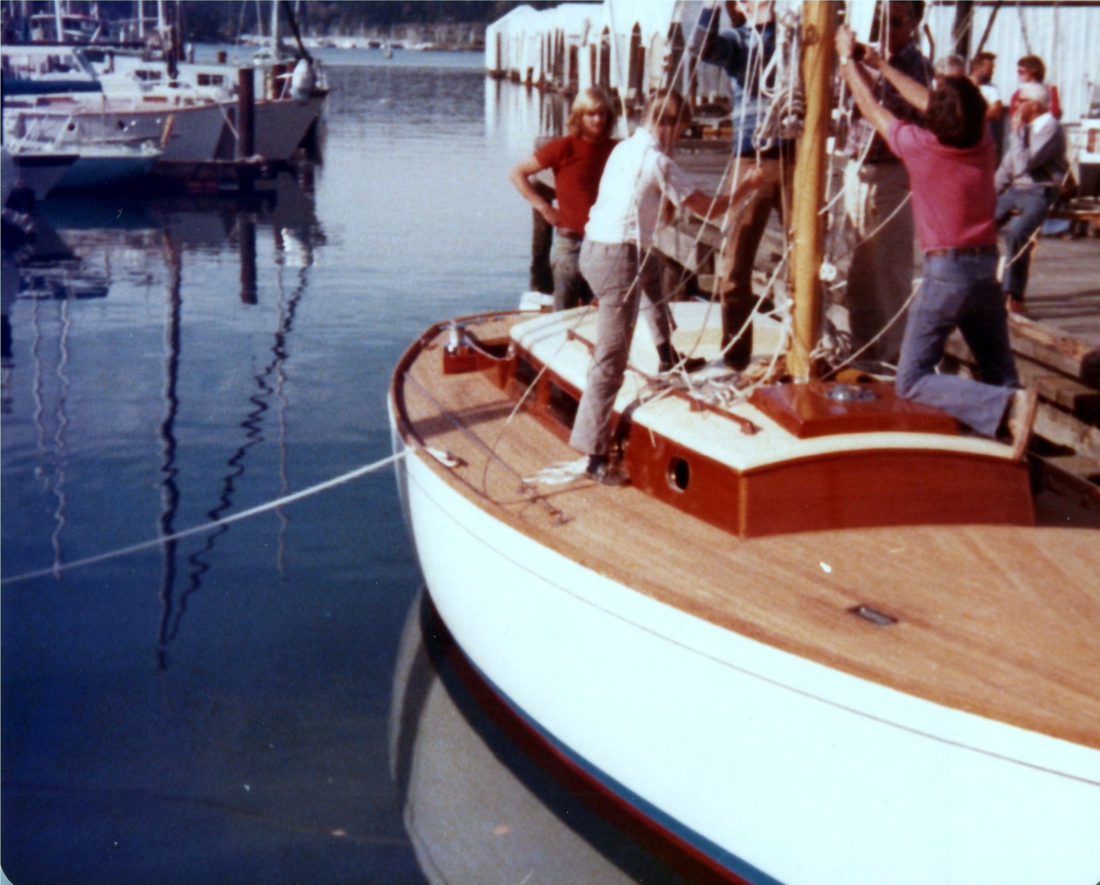 The mast up, men on deck, the boathouses across the water