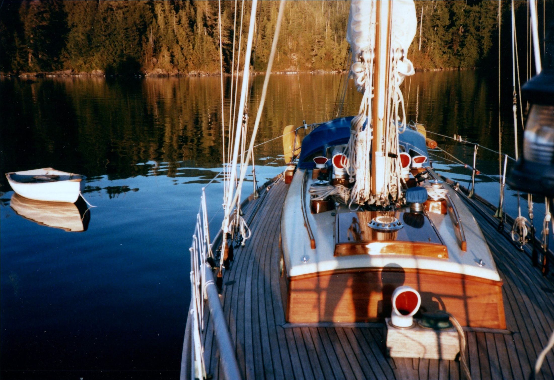 From the bow: the teak deck, the mast and a dinghy astern at anchor